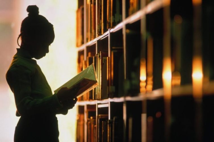 Girl (6-8) looking at book in library, silhouette