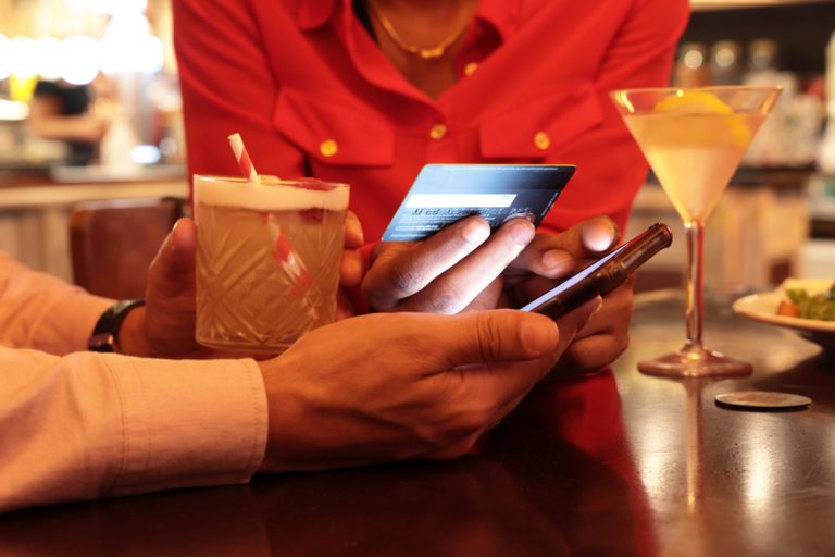 Mixed race couple in bar or cafe using Phone App to pay for drinks and meal